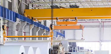 Overhead crane lifting a reel above a paper making production line